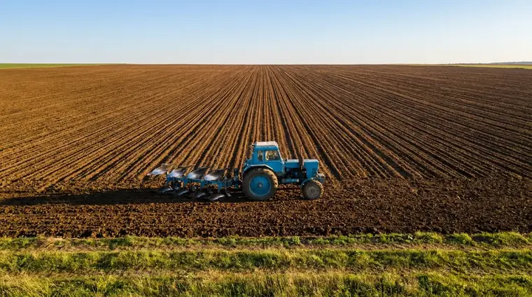 Blue farm tractor ploughing a freshly tilled Indian field
